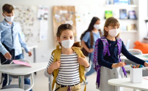 Group of children with face mask back at school after covid-19 quarantine and lockdown. School children in classroom protected by SchoolGuard